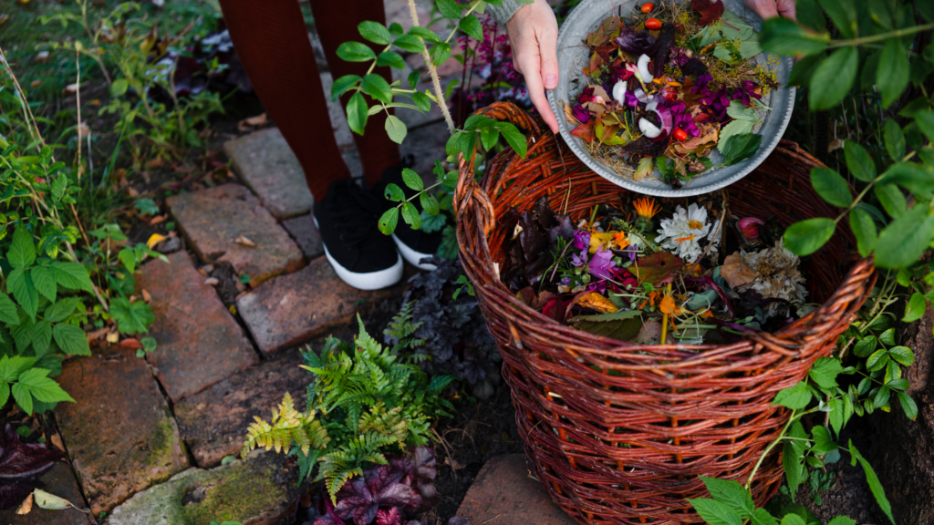 A person adding colorful kitchen scraps, including flowers, leaves, and vegetable peels, into a large woven basket for composting. The image highlights solutions for maintaining a healthy worm bin by focusing on proper food balance and avoiding overfeeding to prevent bad odors.
