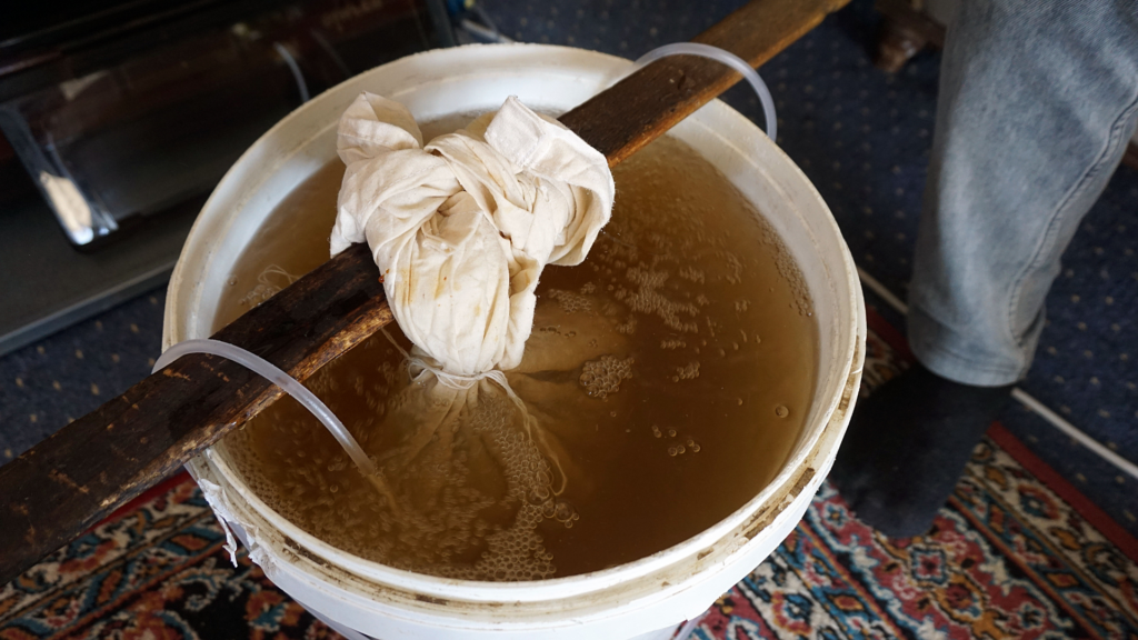 A bucket filled with bubbling water and a cloth bag steeping worm castings, illustrating the process of making nutrient-rich worm tea for gardening.